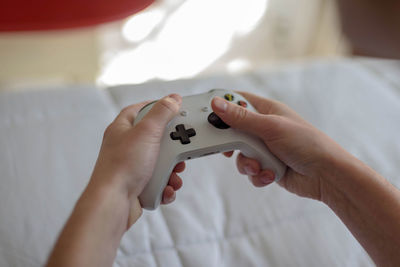 Cropped hands holding game controller on bed at home