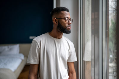Sad black man looking out of window thinking about life problems, dealing with breakup depression