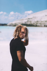 Portrait of man with curly hair standing at beach