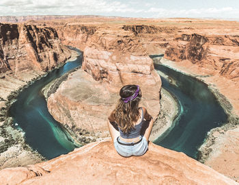 Rear view of man sitting on rock by river