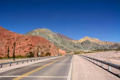 Road by mountain against clear blue sky