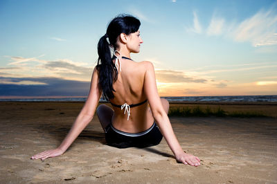 Young woman on beach against sky during sunset