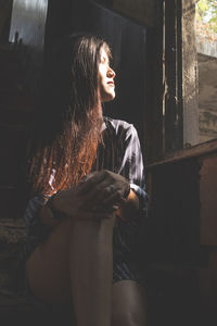 Low angle view of young woman sitting in abandoned building