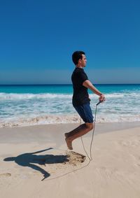 Man  skipping rope on beach against sky