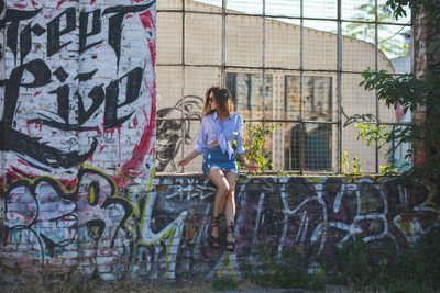 Young woman sitting on window sill amidst graffiti wall