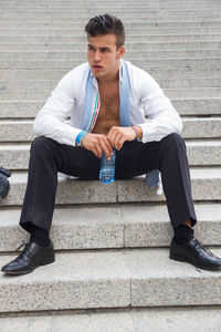 Man looking away while sitting on steps in city