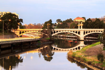 Bridge over river by buildings against sky