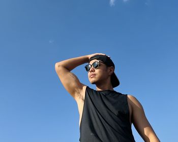 Low angle view of young man wearing sunglasses against blue sky