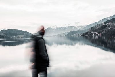 Blurred motion of teenage boys standing at lake against sky