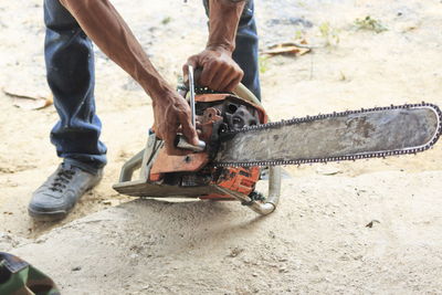 Low section of man holding chainsaw while standing on land 