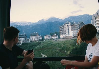 People looking through window at buildings in city