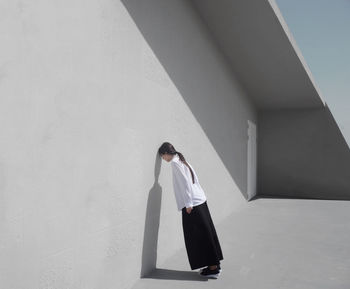 Full length side view of woman leaning on white wall