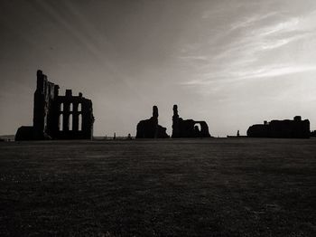 Silhouette buildings on field against cloudy sky