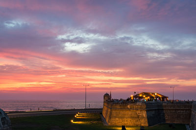 Illuminated historic wall against sea during sunset