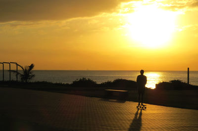 Silhouette man looking at sea against sky during sunset