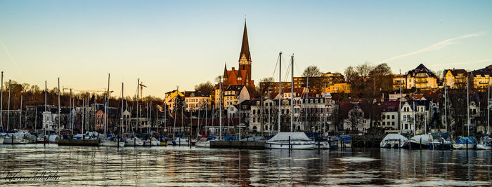 Boats moored in river with buildings in distance