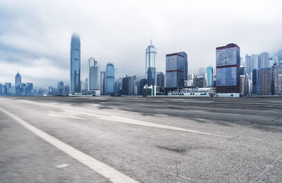 Road by buildings against sky in city