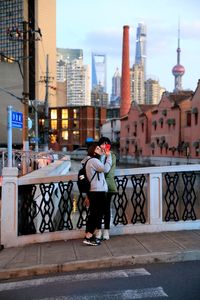 Woman taking selfie with friend on sidewalk in city