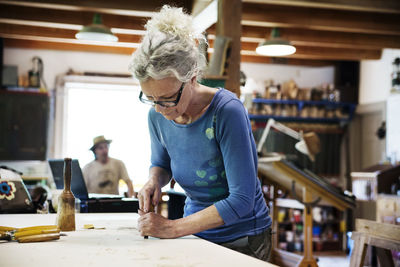 Female craftsperson shaping wood with chisel at table in workshop