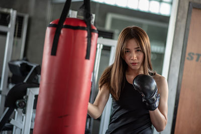 Portrait of confident young woman practicing boxing with punching bag in gym