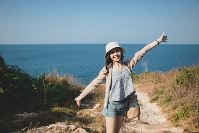 Full length of smiling young woman standing on sea shore against sky