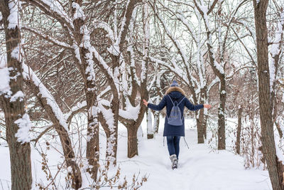 Rear view of woman wearing warm clothing with backpack walking on snow in forest