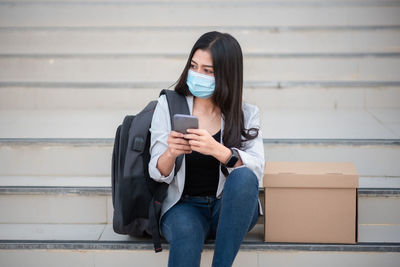 Woman using mobile phone by box on staircase