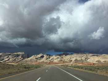 Road passing through landscape against storm clouds