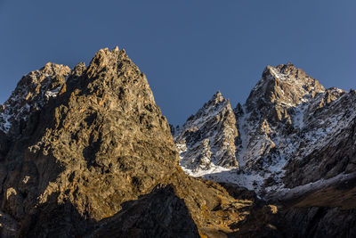 Low angle view of rocky mountains against clear blue sky