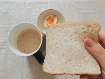 Cropped hand holding bread with coffee and egg on table