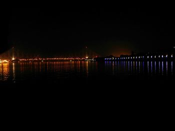 Illuminated bridge over river against sky at night