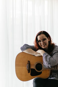 Portrait of young woman sitting on guitar