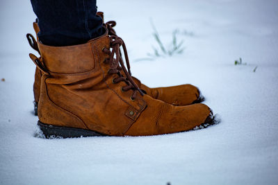 Low section of person wearing leather shoes while standing on snow