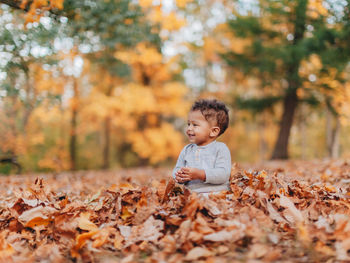 Cute smiling boy sitting on autumn leaf in forest