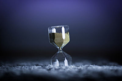 Close-up of hourglass on table against blue background