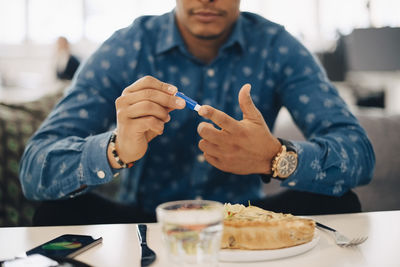 Midsection of businessman doing blood test while having food at table