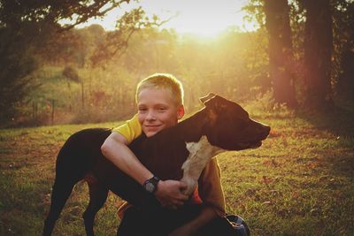 Summertime backlit portrait of teenage boy and his dog with scenic landscape. 