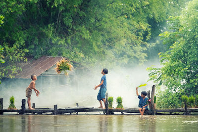 Siblings on footbridge over lake in forest