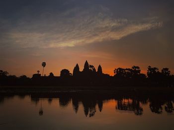 Silhouette temple by lake against sky during sunset