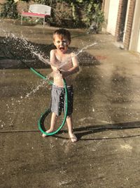 Full length of shirtless boy holding water pipe standing outdoors