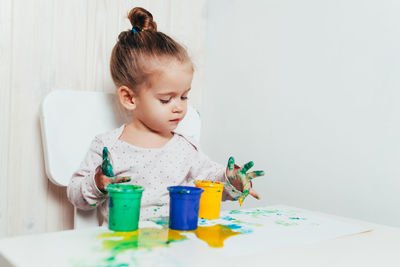 Cute baby girl sitting with paper and paints at table