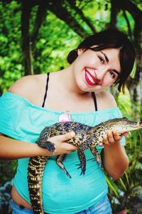 Portrait of smiling young woman holding crocodile in zoo