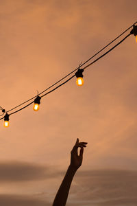 Silhouette person holding light bulb against sky during sunset