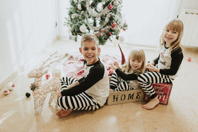 Happy girls and boy decorating christmas tree at home