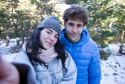 Portrait of young couple wearing warm clothing standing in forest during winter