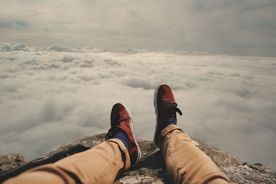 Low section of man on rock against cloudy sky