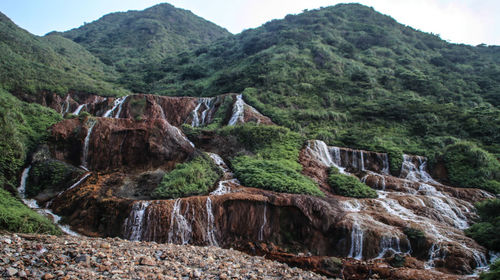 Scenic view of waterfall by mountains against sky