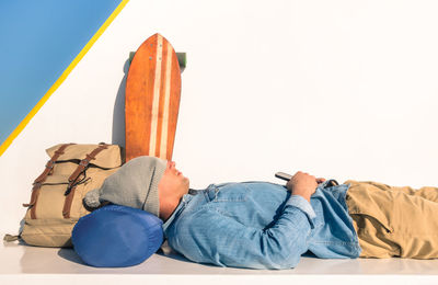 Side view of man sleeping by backpack and skateboard