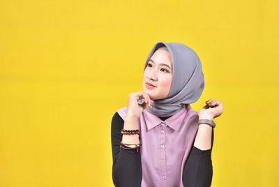 Young woman standing against yellow background