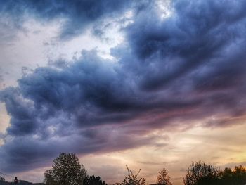 Low angle view of trees against dramatic sky